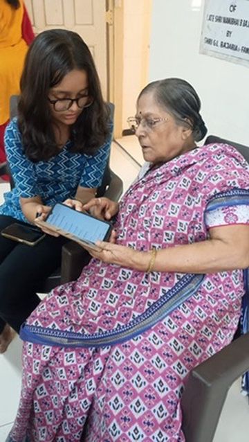 A female Tech Mitra volunteer showing a tablet to an elderly woman during a one-on-one session